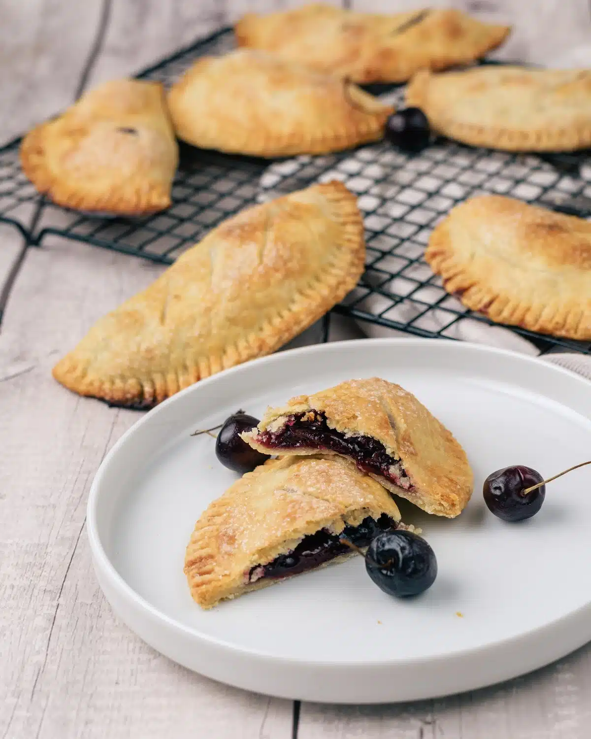 A cherry hand pie on a white plate with fresh cherries, split to show the jammy filling inside