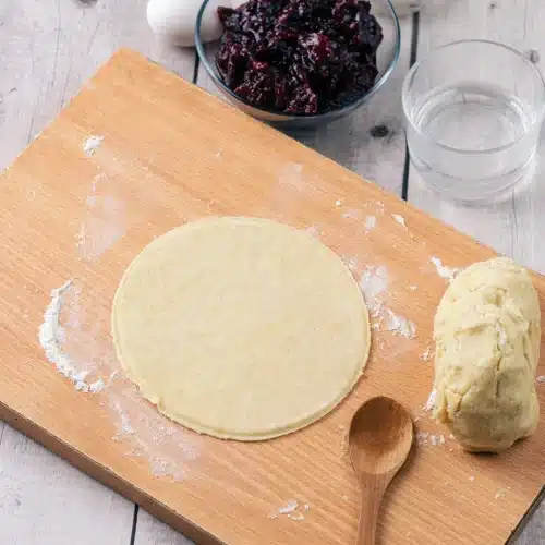 A round of pastry cut on a floured board beside the ball of dough