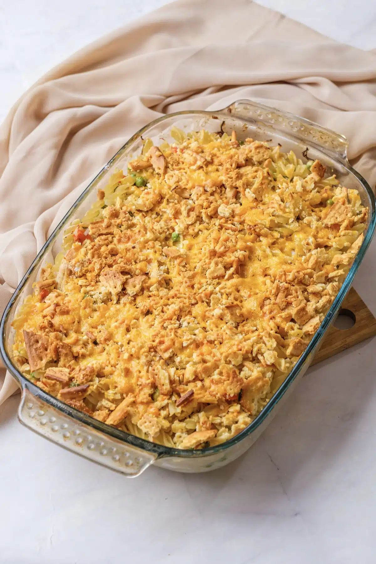 Creamy chicken noodle casserole in a glass dish with a golden cheddar and cracker topping on a beige cloth