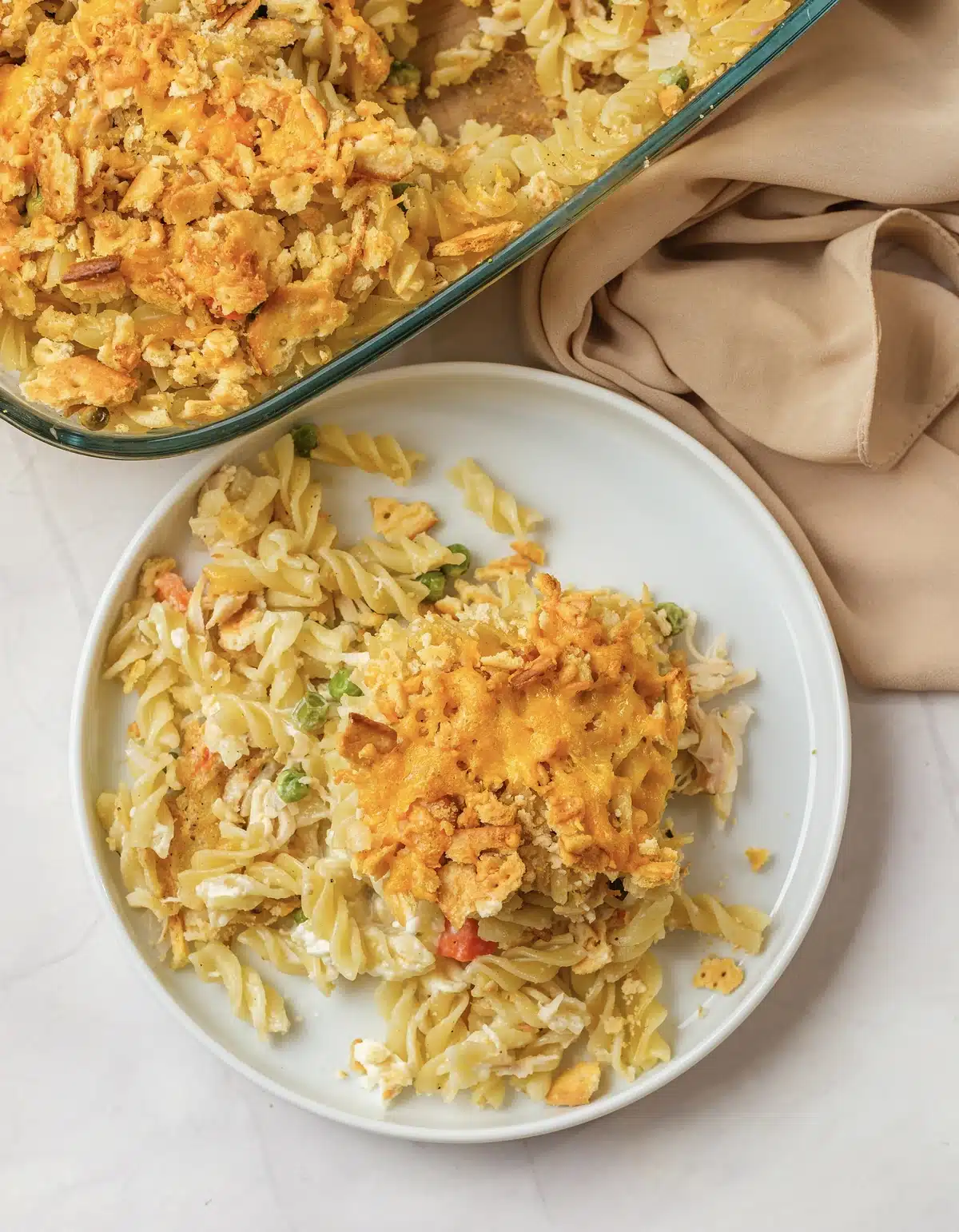 A plated serving of pasta and chicken with the golden topping beside the glass baking dish