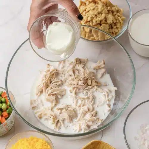 Sour cream tipped from a small glass into the bowl of chicken and soup