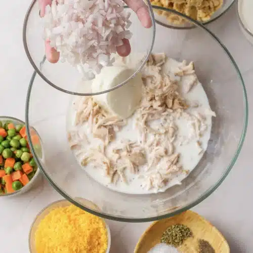 Diced onion added from a glass bowl to the creamy chicken mixture