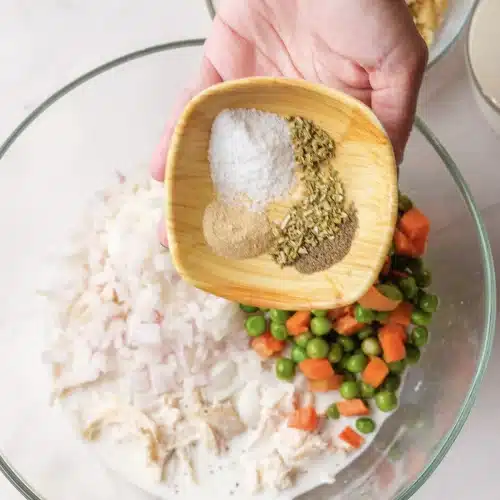 Garlic powder, parsley, salt and pepper tipped from a wooden dish into the bowl with the peas and carrots