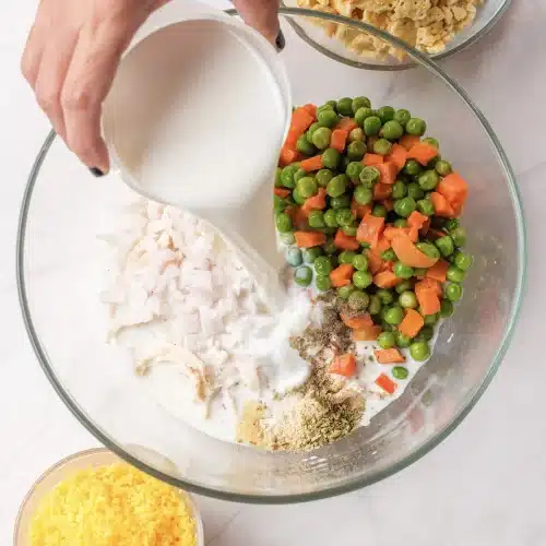 Milk poured from a glass into the bowl of chicken, peas and carrots