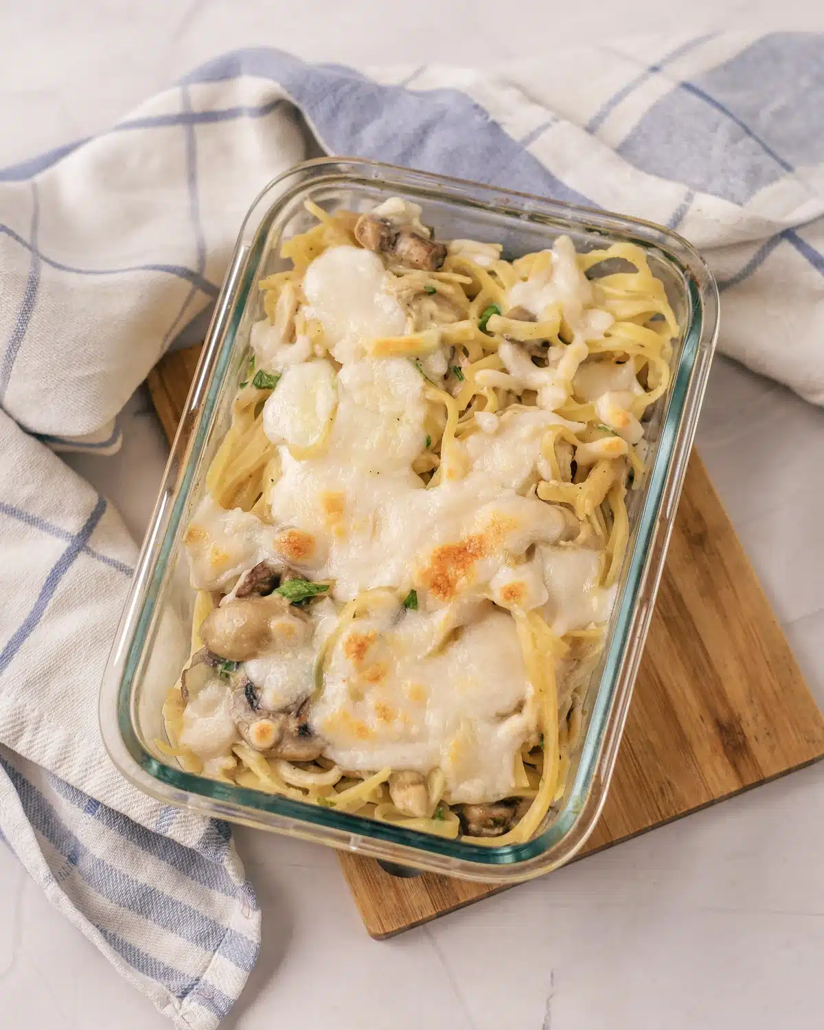 Chicken tetrazzini in a glass baking dish with browned mozzarella, mushrooms and parsley on top
