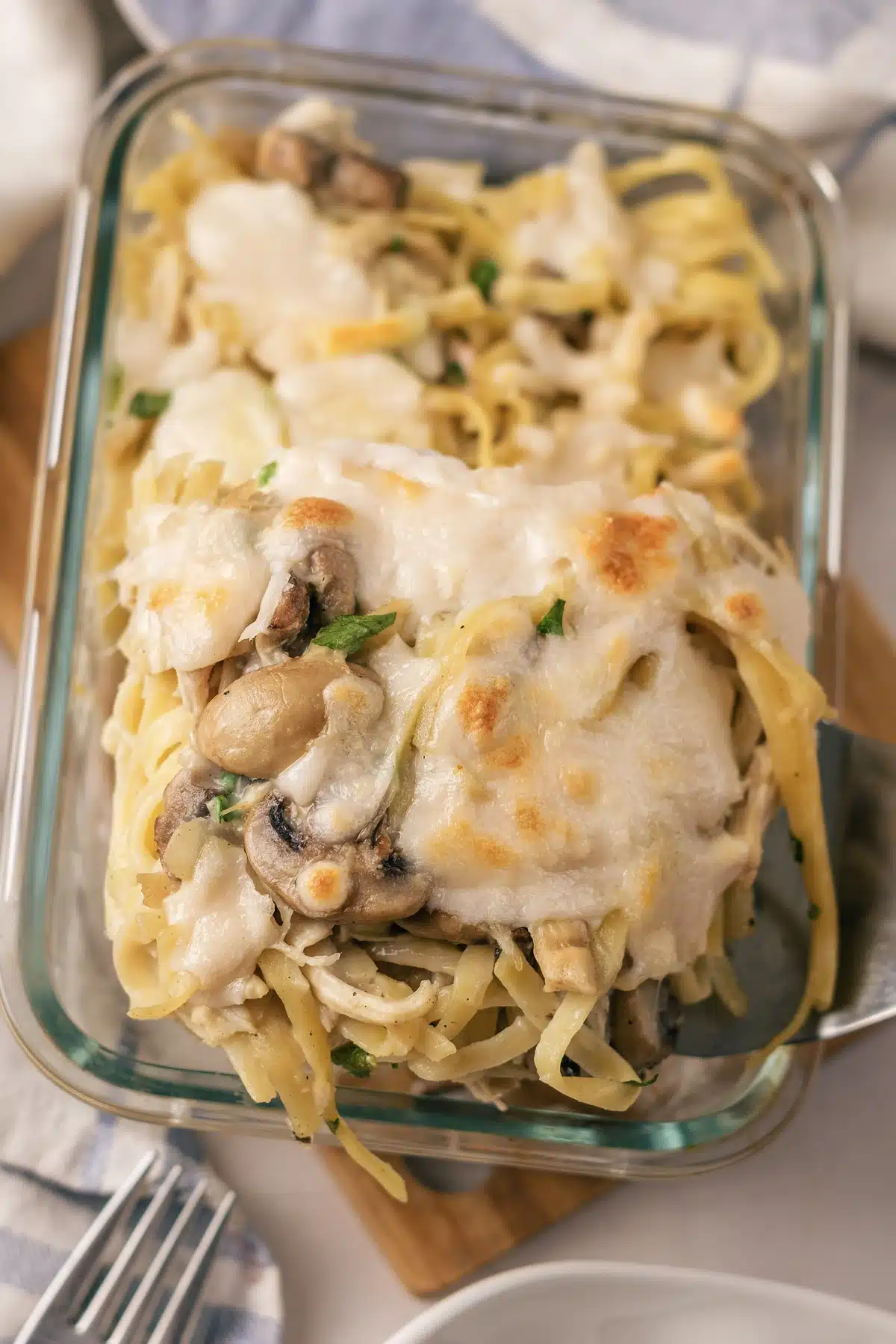 A spatula lifting a square of baked pasta with mushrooms out of the corner of the glass dish
