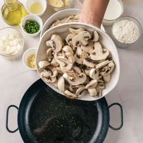 Sliced mushrooms tipped from a bowl into a dark skillet