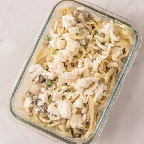 The pasta, mushroom and chicken mixture in a glass dish topped with shredded mozzarella, ready to bake
