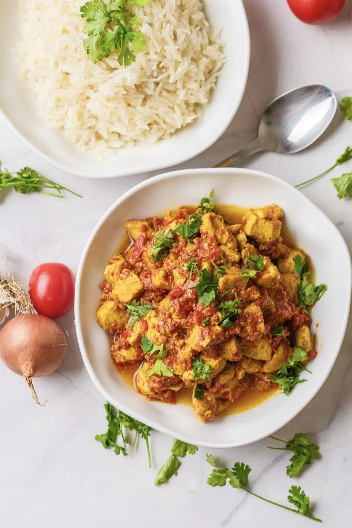 Chicken tikka masala with a thick tomato sauce and fresh cilantro on a white plate, with basmati rice behind