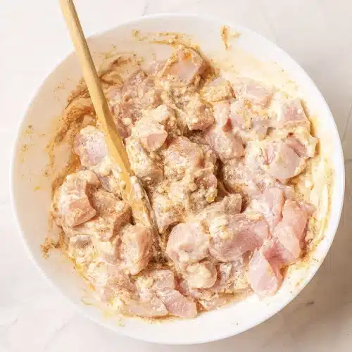 The cubed chicken stirred with a wooden spoon until coated in the spiced yogurt marinade