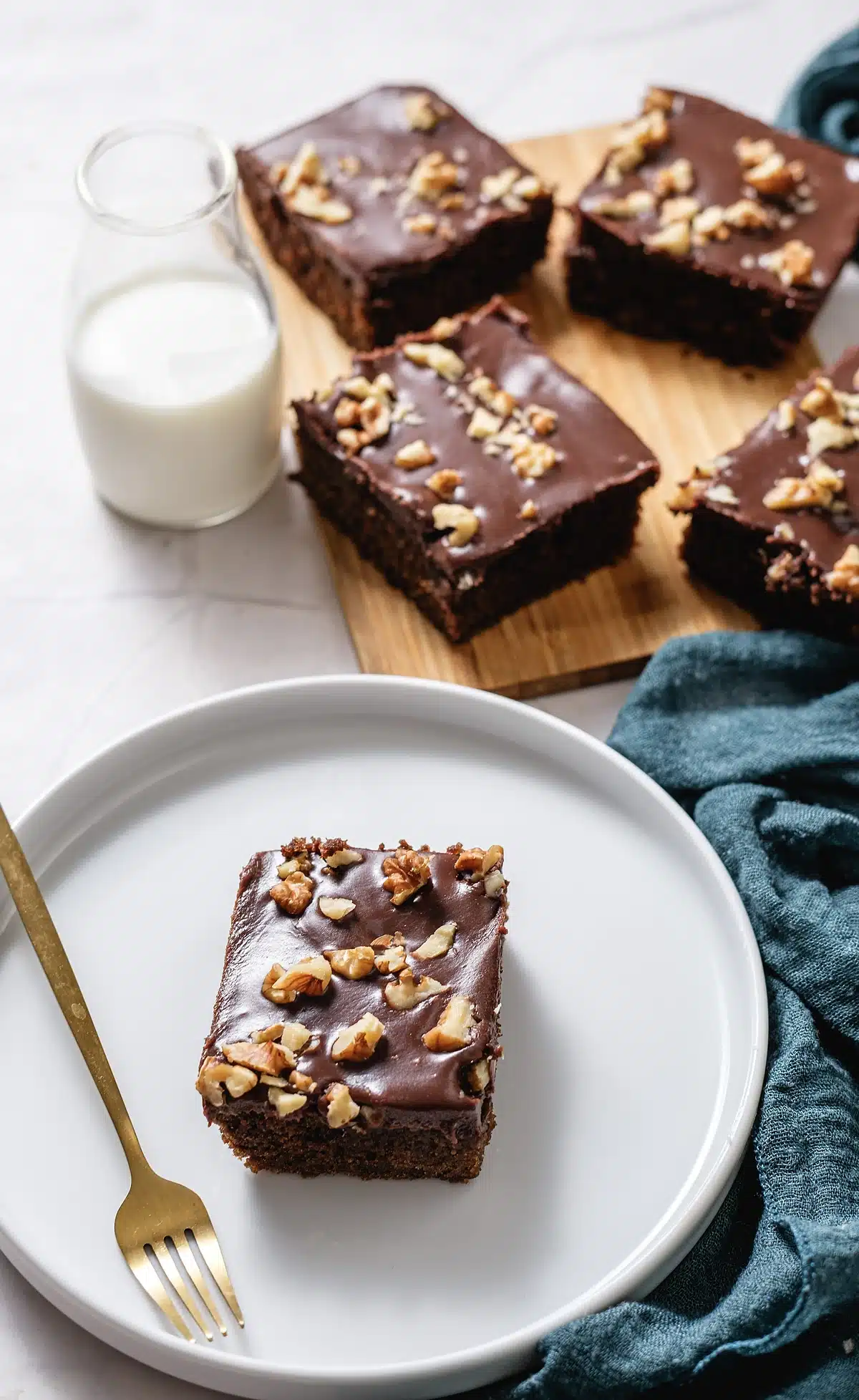 Chocolate buttermilk cake squares with a glass of milk and a teal napkin