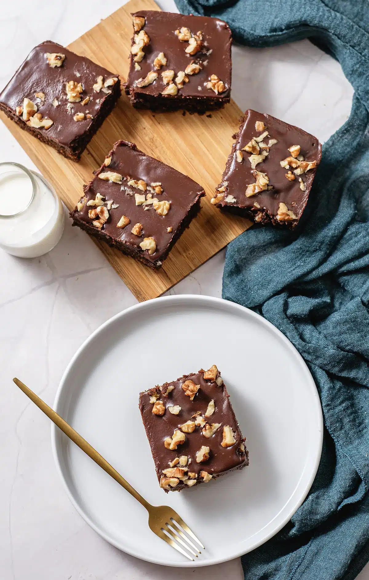 Chocolate buttermilk cake squares on a board with a plated slice and a gold fork