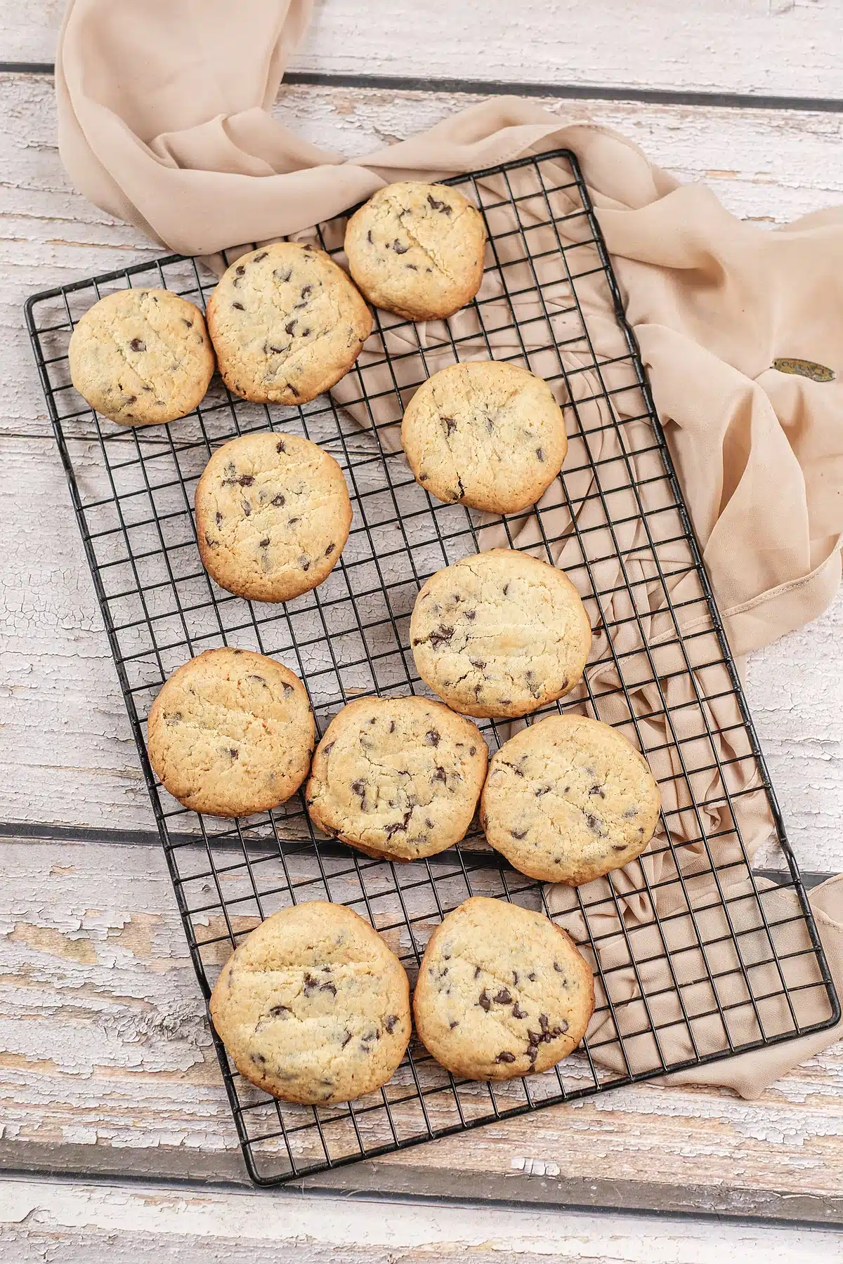 Chocolate chip pudding cookies spread across a rack on a white wooden table