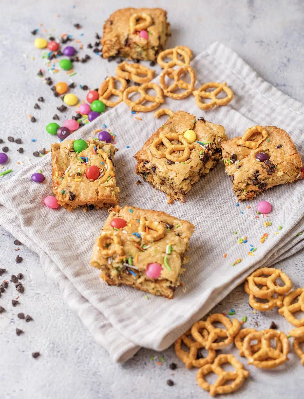 Cut squares scattered on a cloth with mini pretzels and candy, seen at an angle