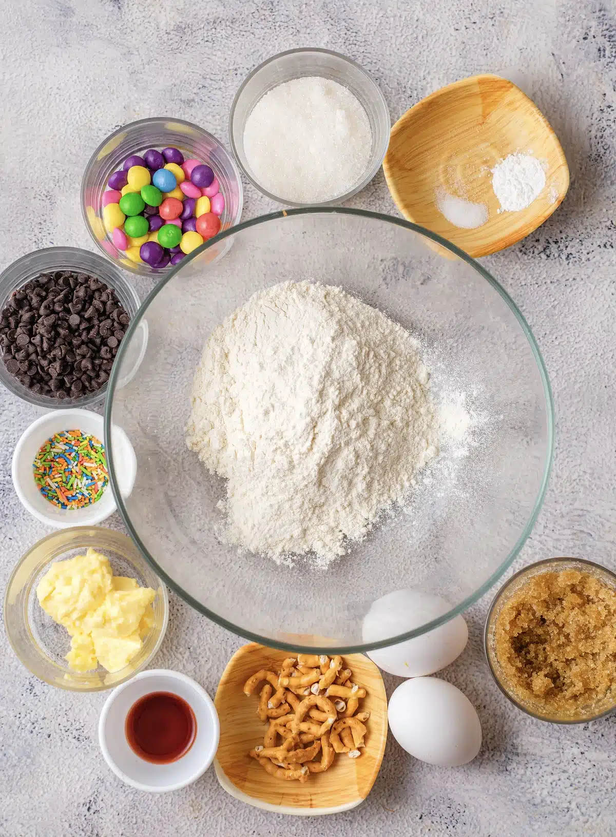 Ingredients for Christmas cookie bars: flour, butter, brown and white sugar, eggs, vanilla, mini chocolate chips, rainbow candy, sprinkles and pretzels