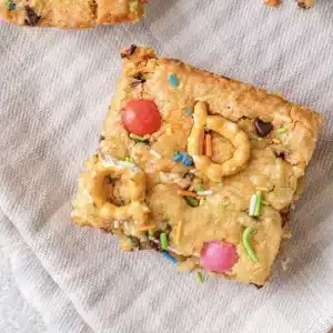 A single square of Christmas cookie bars, rainbow version, on a striped cloth