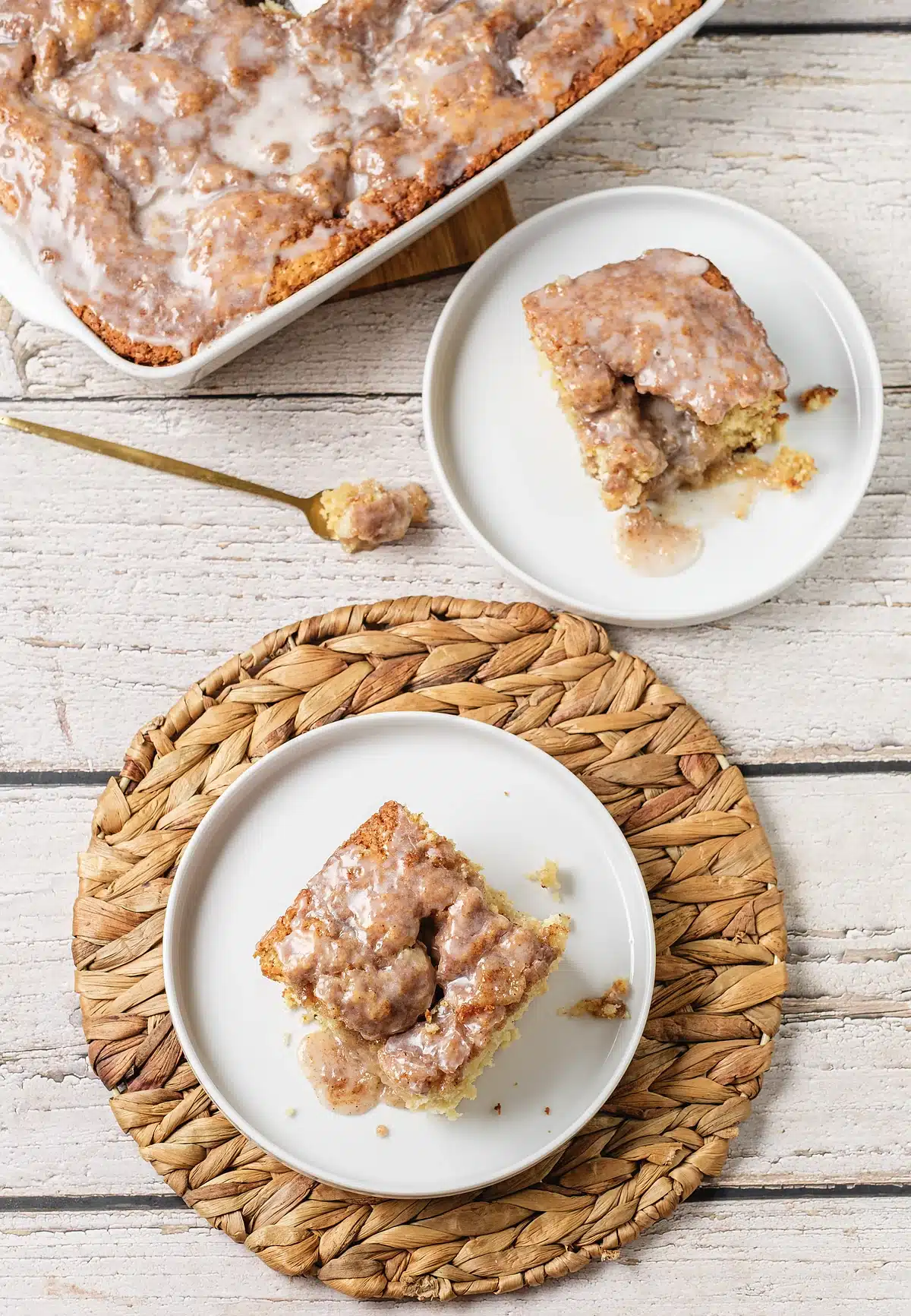 Cinnamon roll coffee cake plated twice beside a pale wooden board