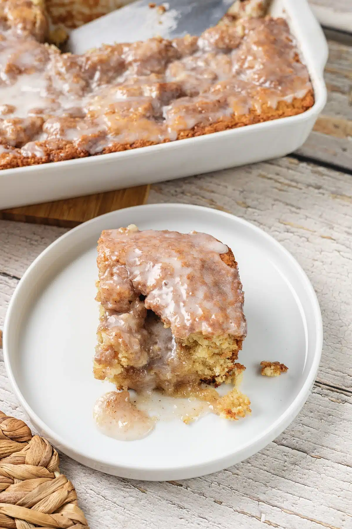 Cinnamon roll coffee cake on a plate with the baking dish behind it