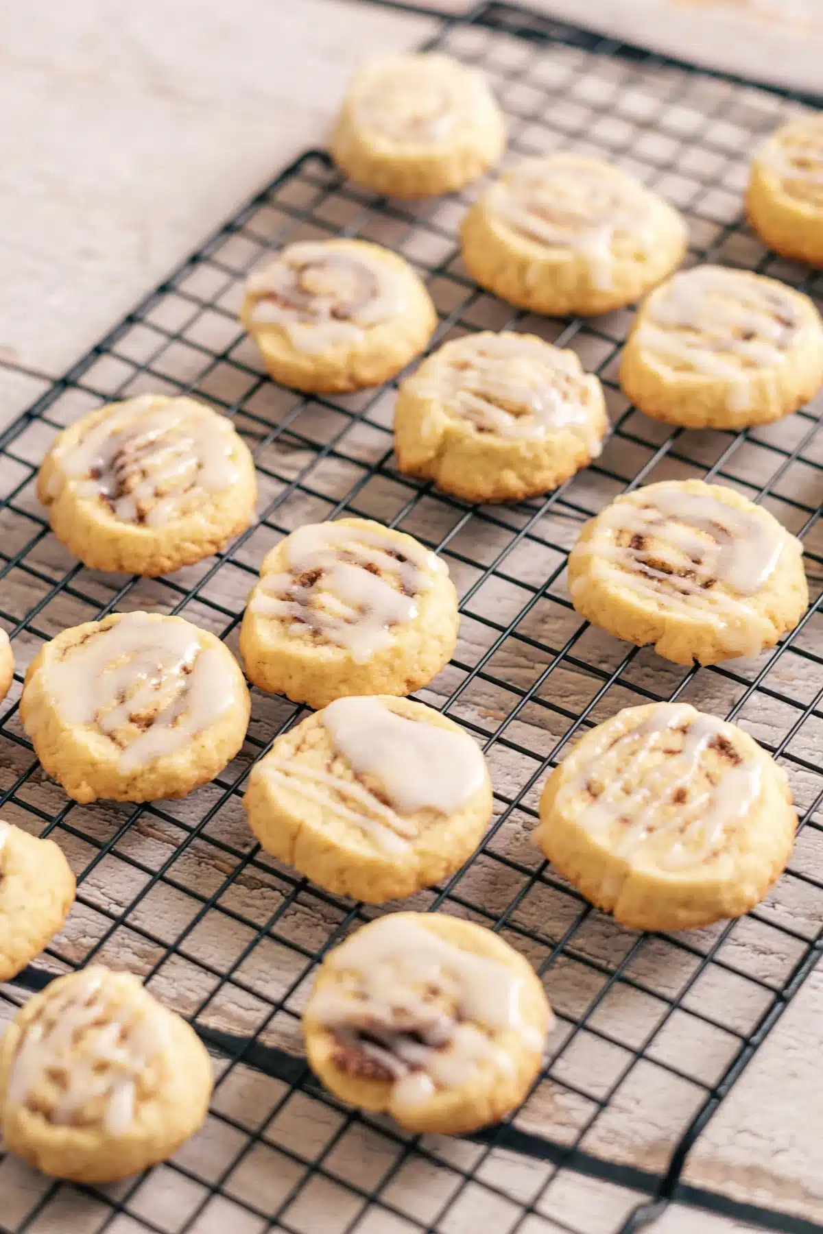 Cinnamon roll cookies with a white glaze cooling on a black wire rack
