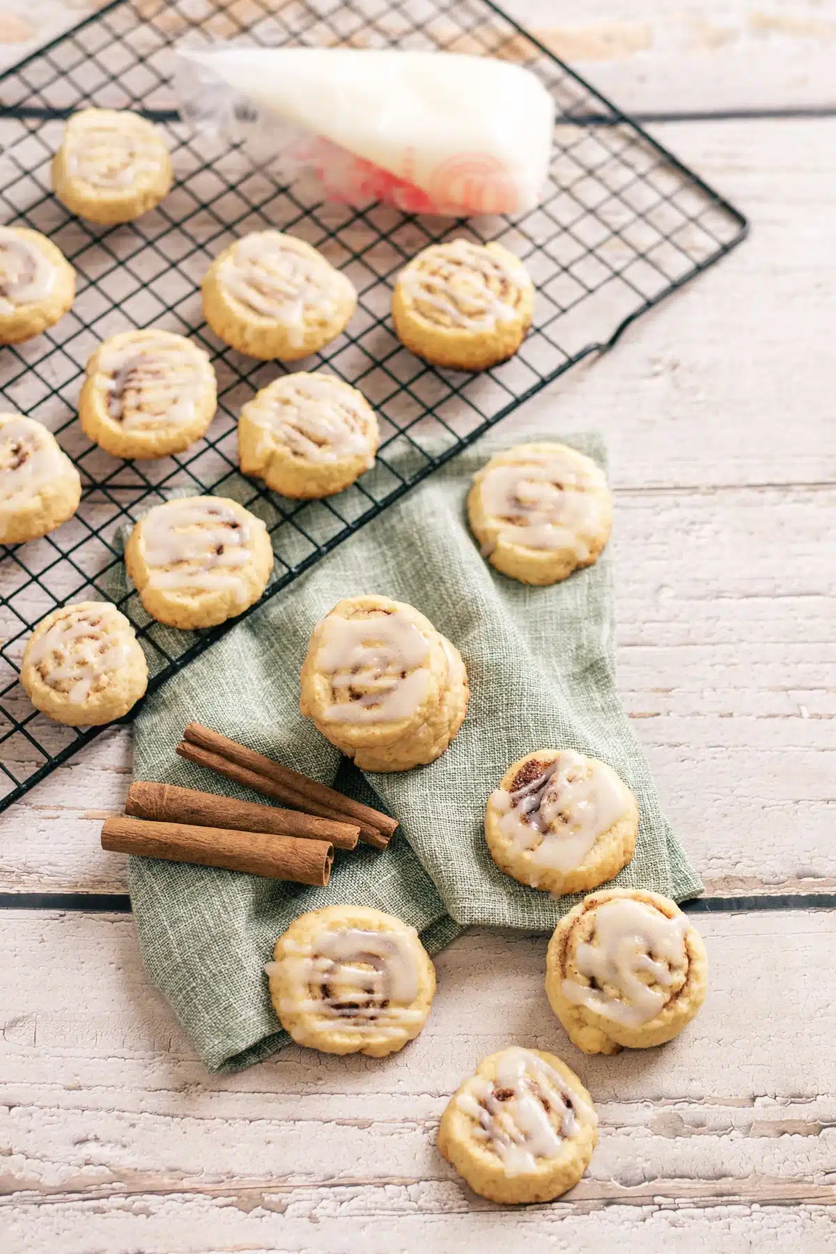 Cinnamon roll cookies on a wire rack and a green napkin with a piping bag and bark sticks nearby