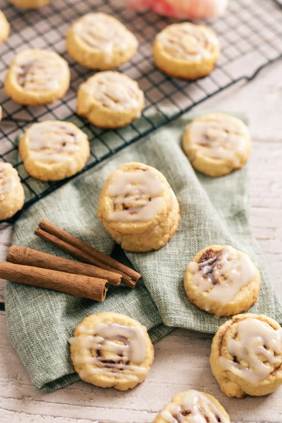 Cinnamon roll cookies with a piped white glaze on a green napkin with two bark sticks beside them