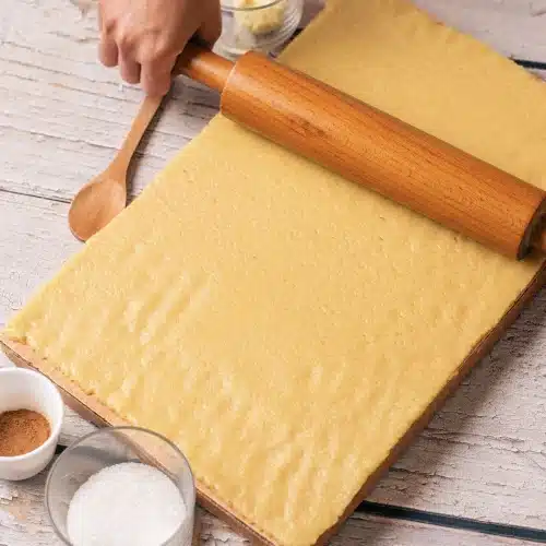 The dough rolled into a rectangle on parchment with a wooden pin