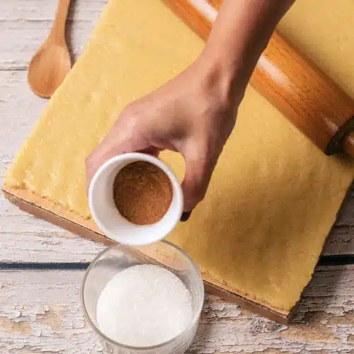 Ground spice tipped into a bowl of sugar beside the rolled dough