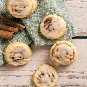 A few cinnamon roll cookies with a piped white glaze on a green napkin, seen from above