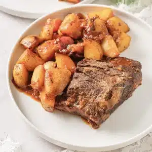 A single serving of classic pot roast with potatoes on a white plate