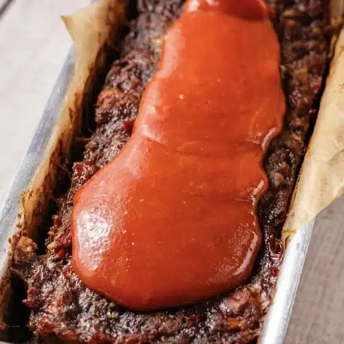 Red glaze pooled along the top of a baked loaf in its metal pan