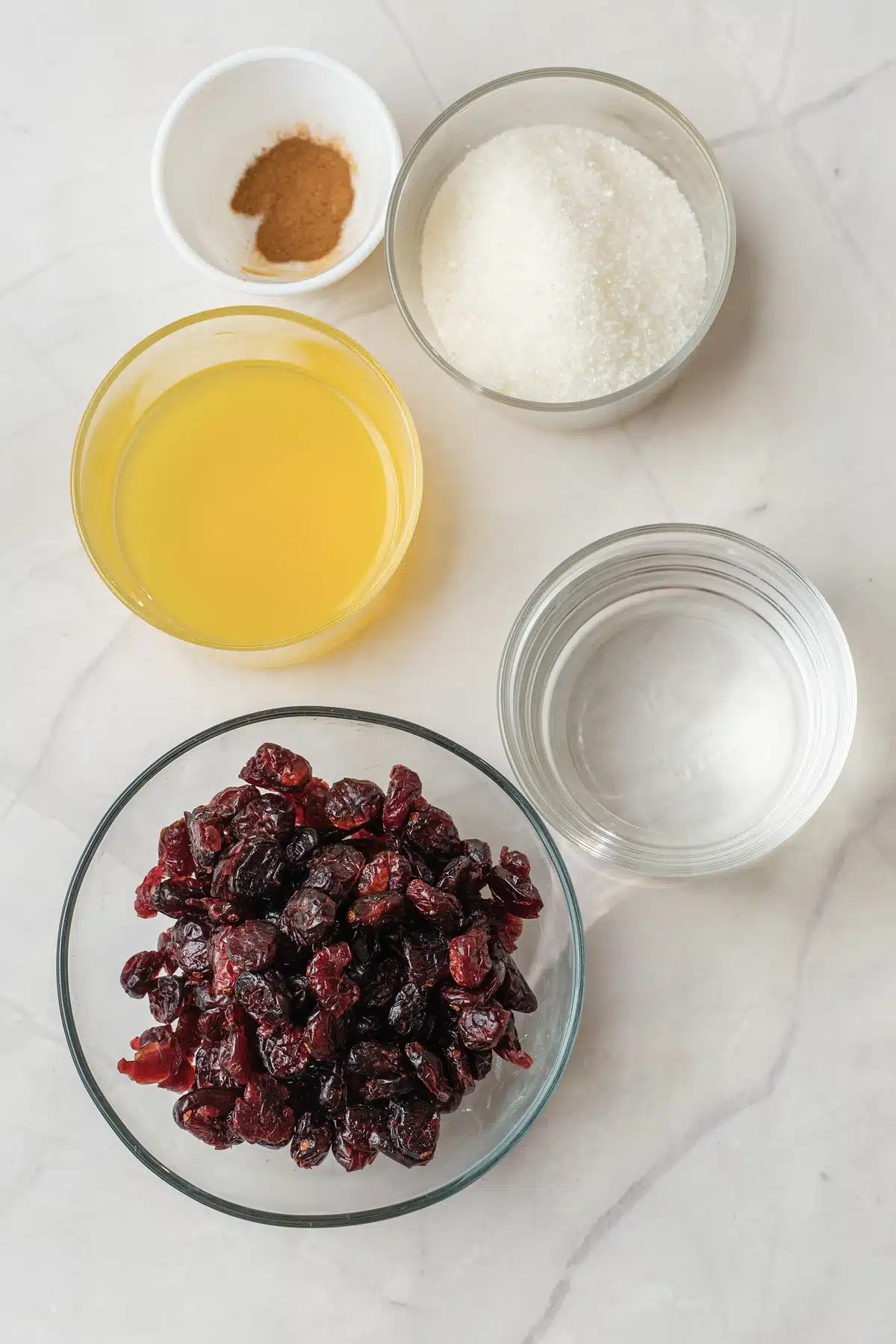 Ingredients for the dried cranberry version of this cranberry sauce: dried cranberries, orange juice, sugar, water and ground cinnamon in small bowls