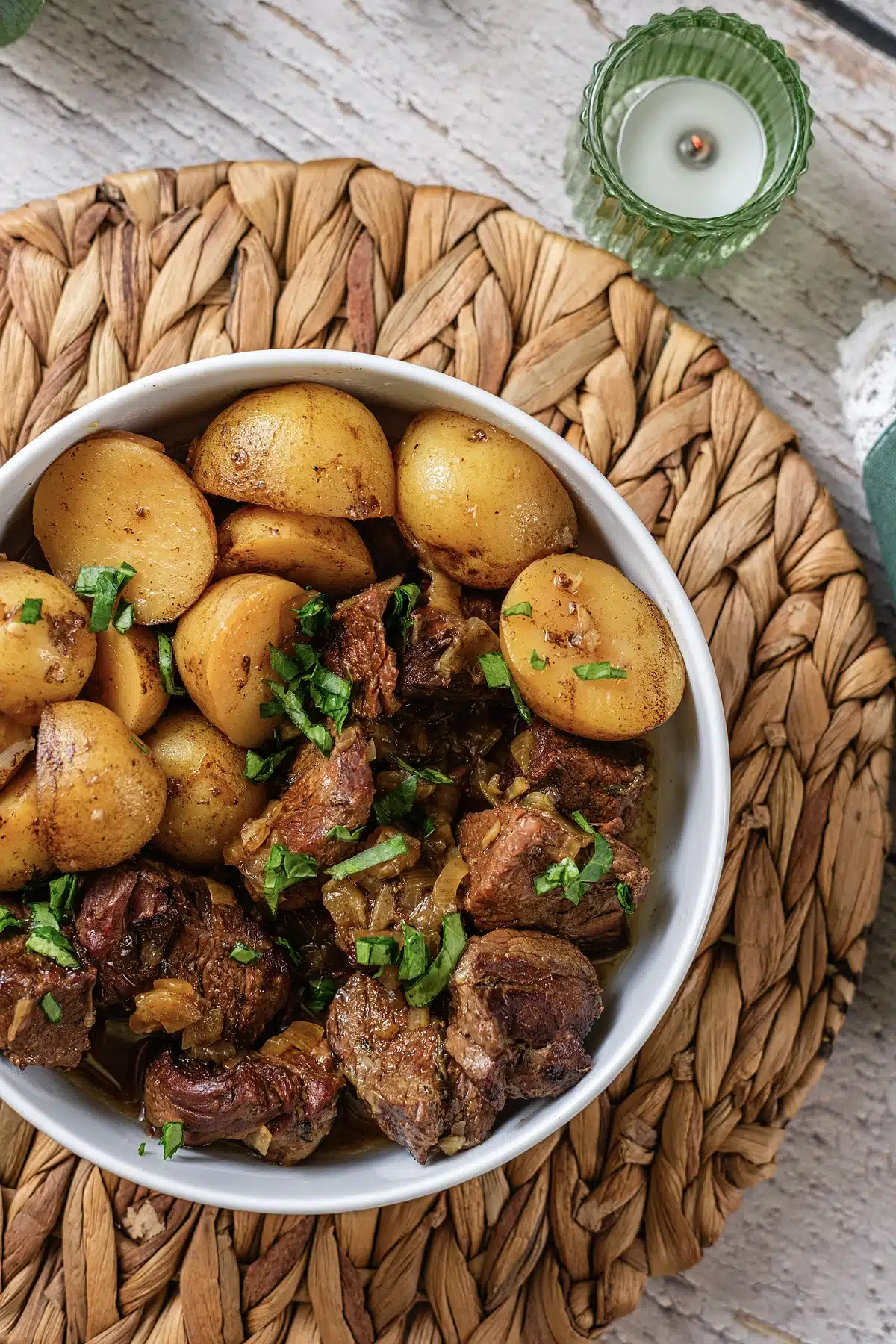A close overhead bowl of glossy beef chunks and golden halves scattered with herbs