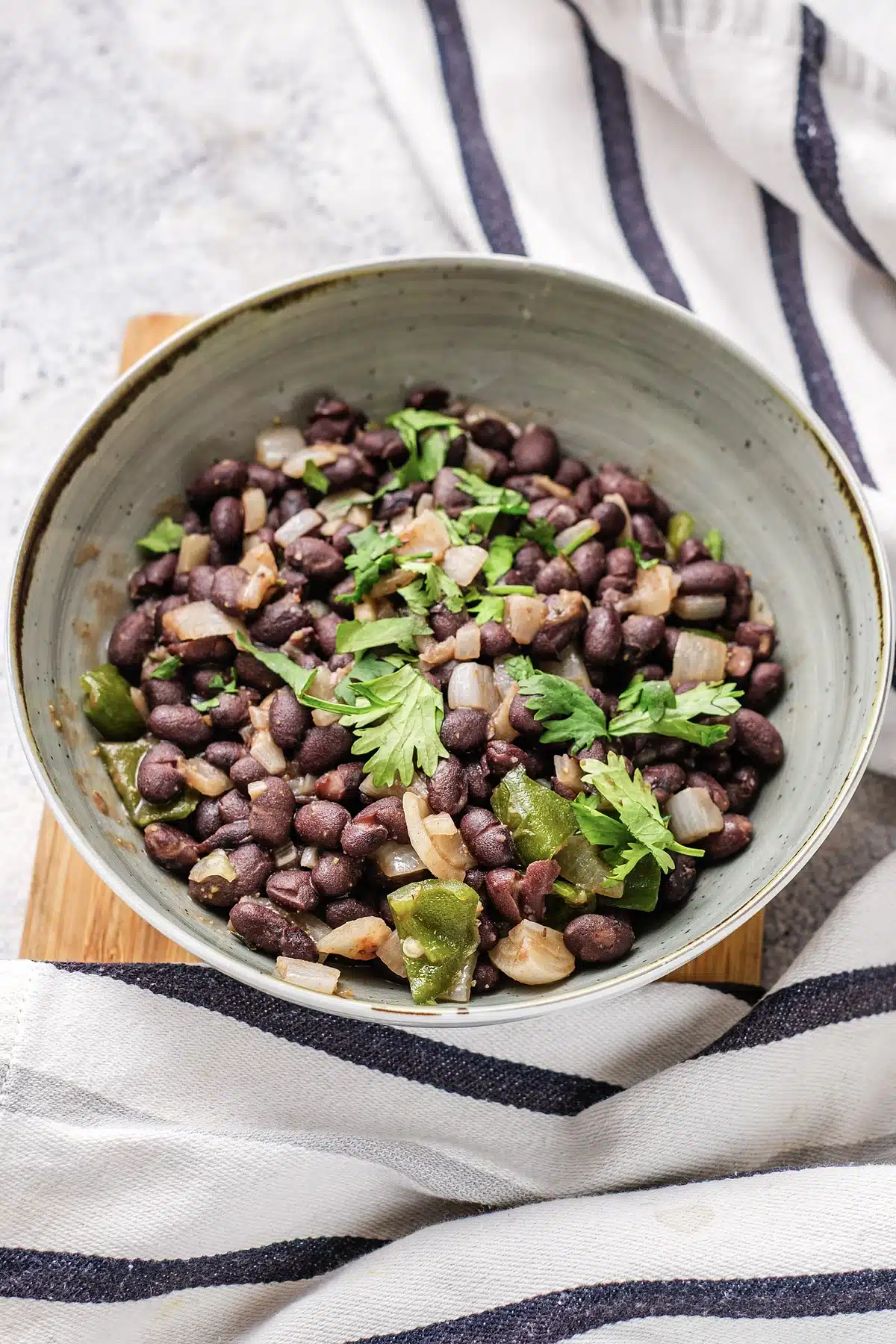 A rustic gray bowl on a wooden board over a striped cloth
