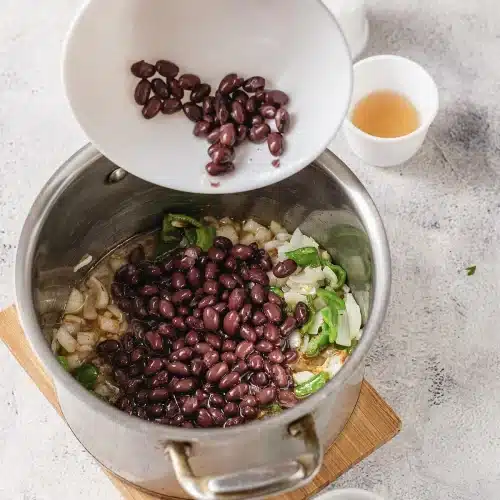Dark legumes tipped from a bowl into the pot of softened sofrito
