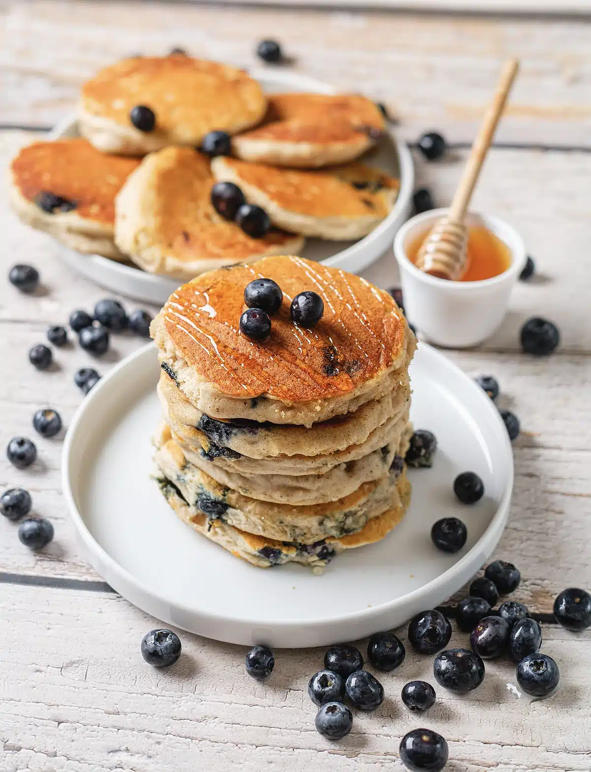 Fluffy blueberry pancakes on a white plate with a honey dipper alongside