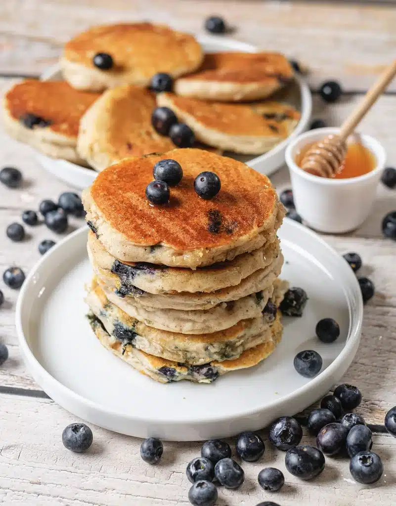 Fluffy blueberry pancakes on a white plate with a pot of honey behind