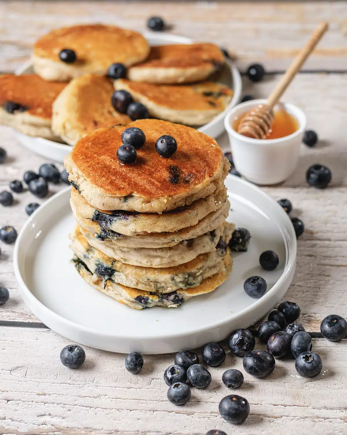 Fluffy blueberry pancakes seen from the side with berries scattered around