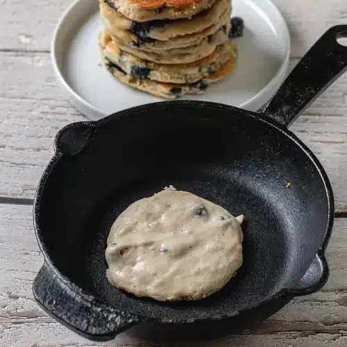 A ladle of batter dropped into a black cast iron pan