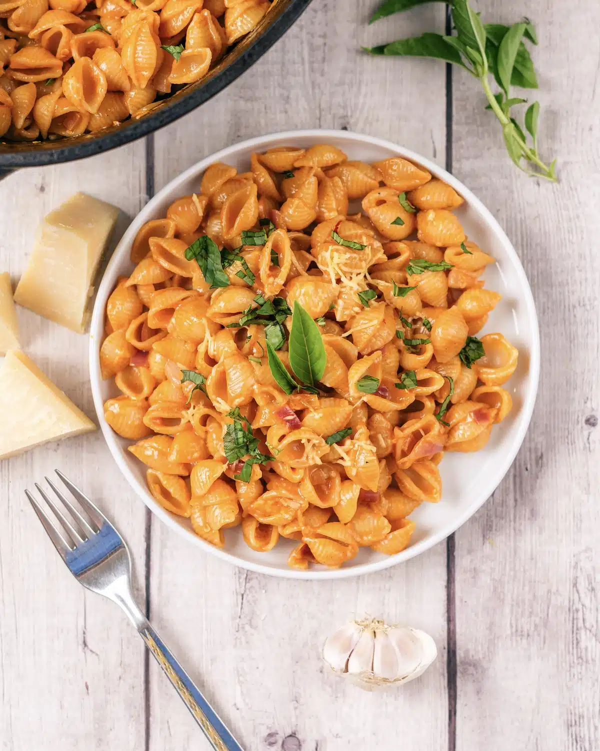 Gigi Hadid pasta served on a white plate with a fork, a wedge of Parmesan and a head of garlic alongside