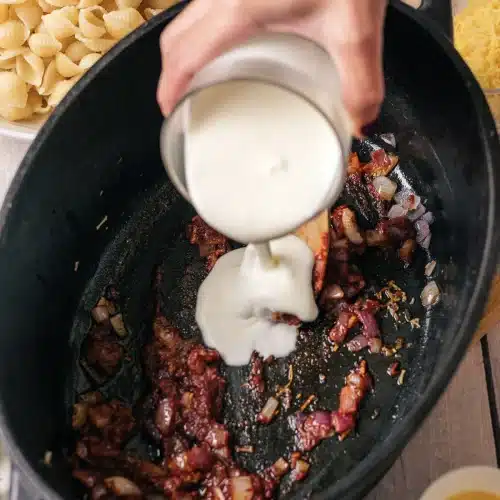 Heavy cream poured into a black skillet over cooked onion and darkened tomato paste