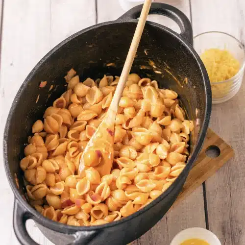 Cooked shells stirred through the orange sauce in the skillet with a wooden spoon