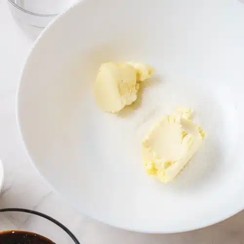 Softened butter and sugar in a white mixing bowl ready to be creamed