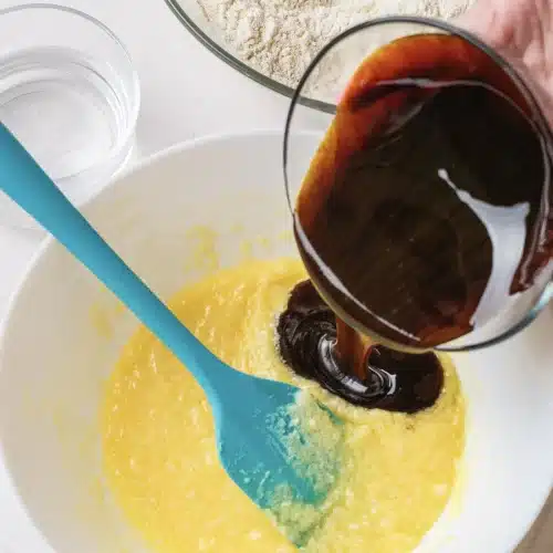 Molasses poured from a glass into the creamed butter and egg mixture