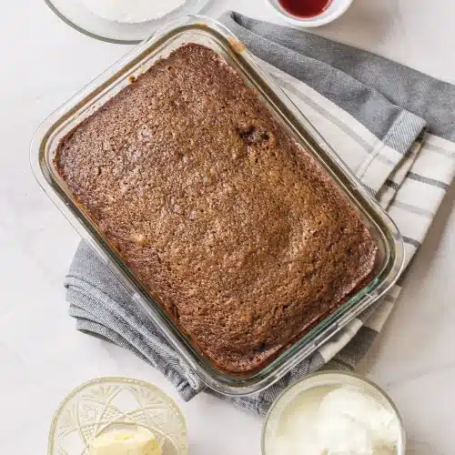 The baked slab in a glass dish on a striped towel with whipped cream and sauce alongside