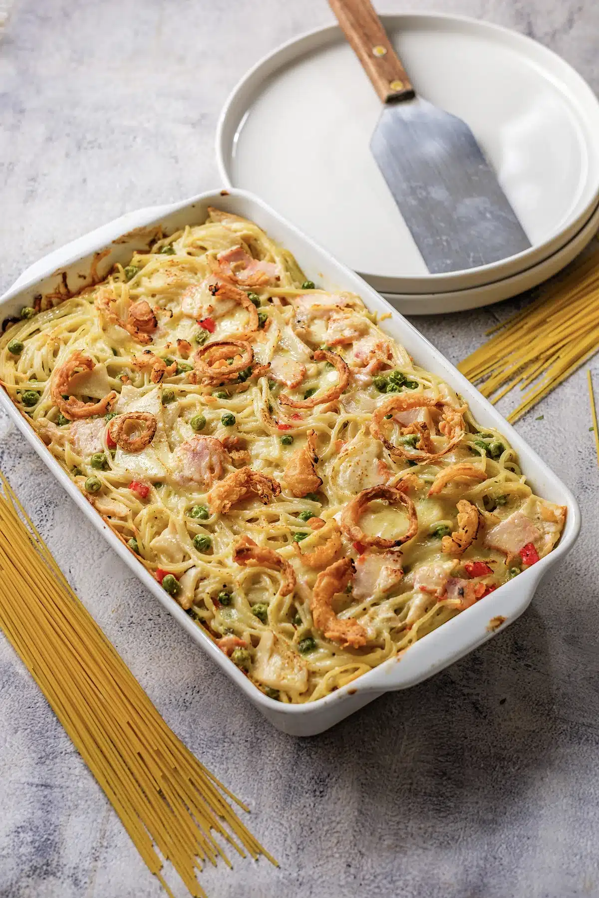 A rectangular casserole dish beside stacked plates and dry spaghetti