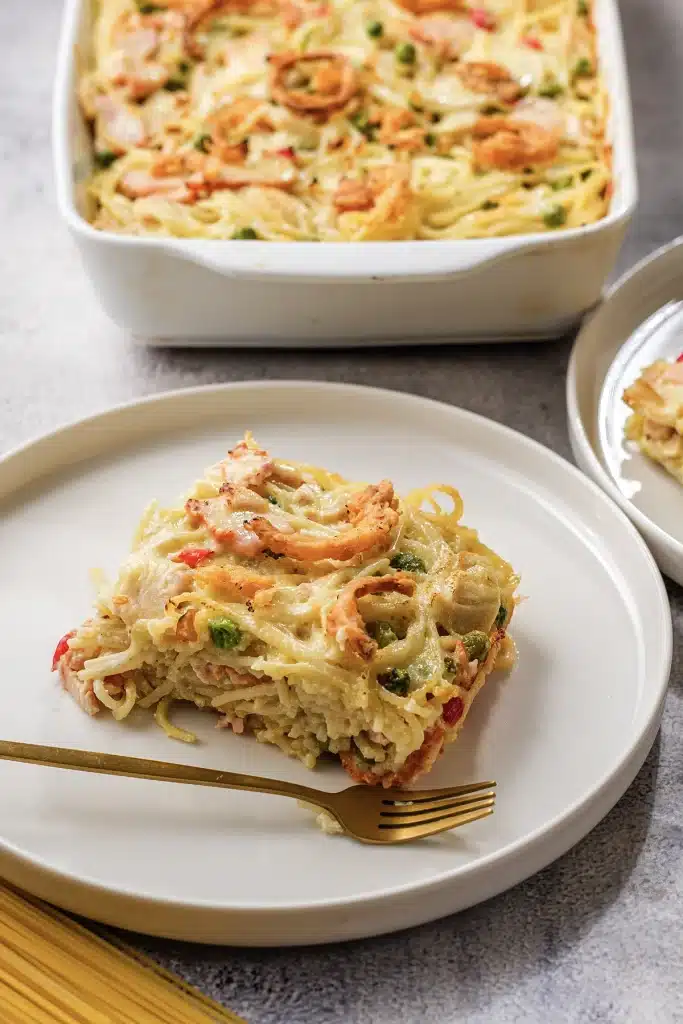 Ham tetrazzini served on a white plate with the dish behind and a gold fork