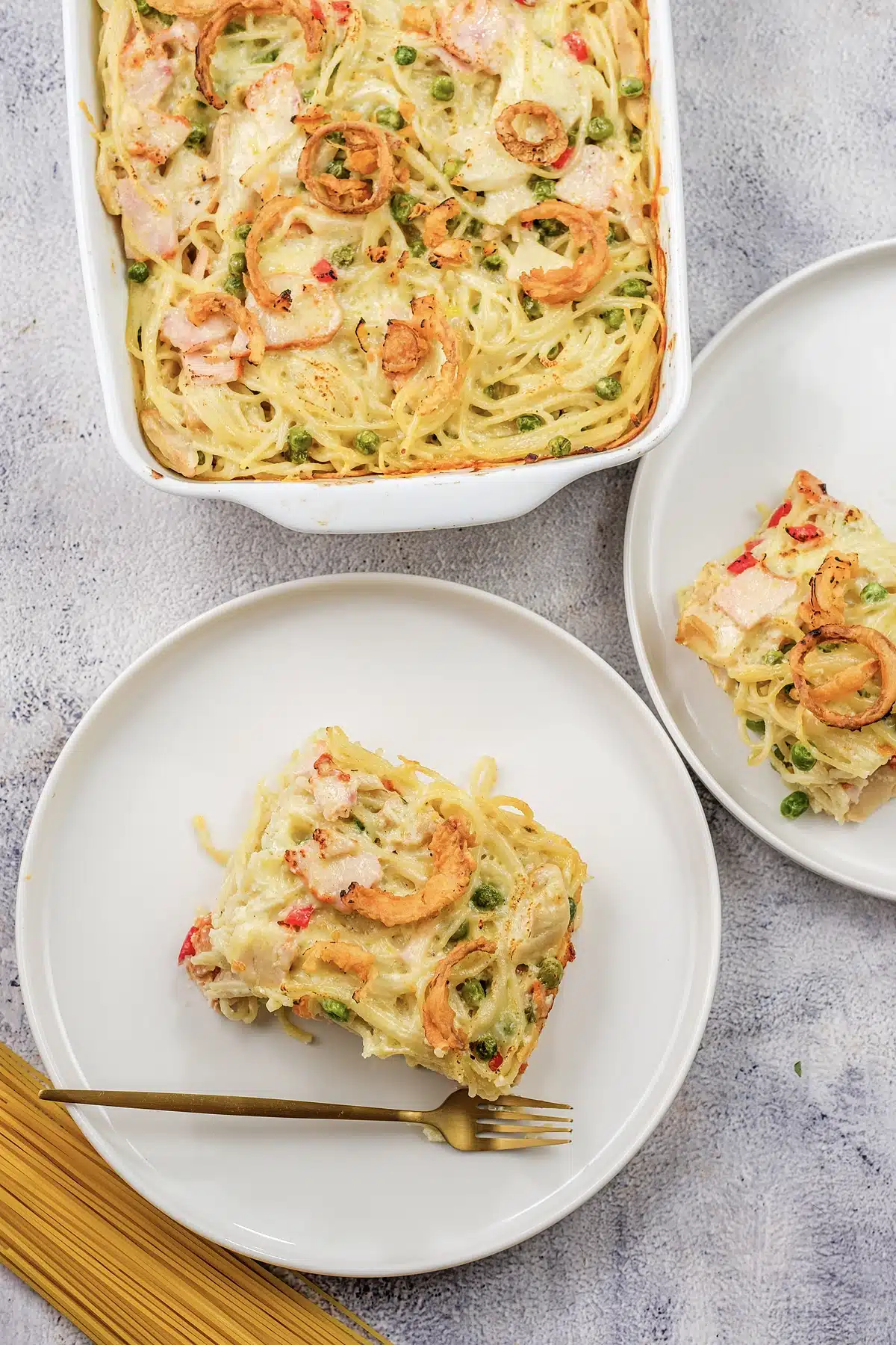 A square of baked ham tetrazzini on a white plate with a gold fork