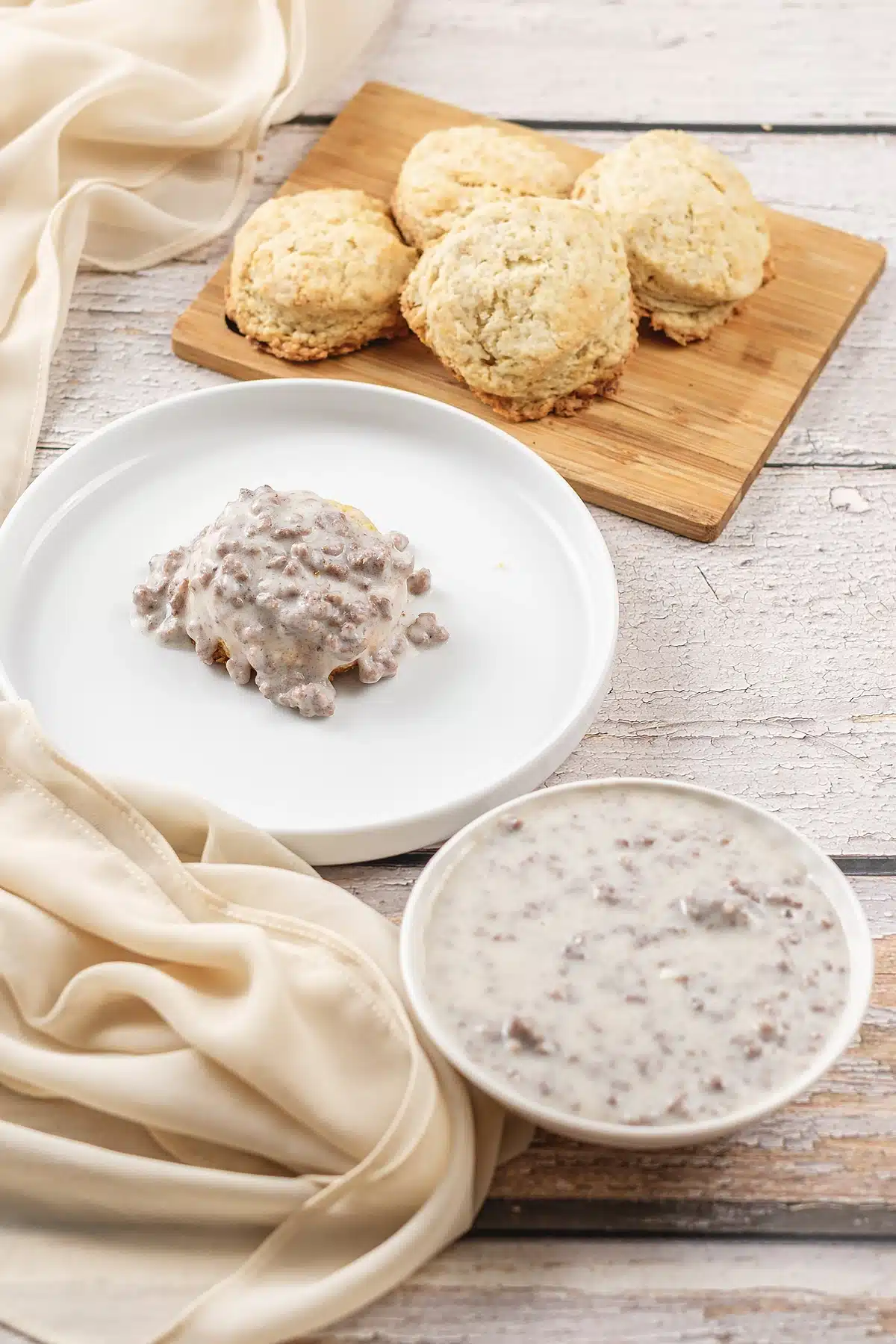 A plate of biscuit under creamy white sauce beside a bowl of more of it