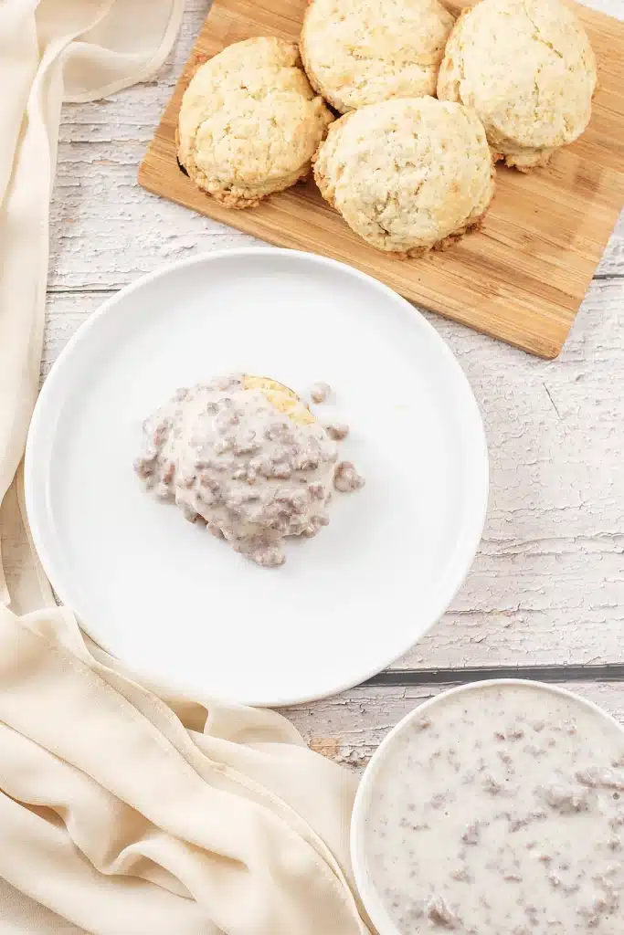 Sausage gravy on a plate seen from directly above with warm biscuits behind
