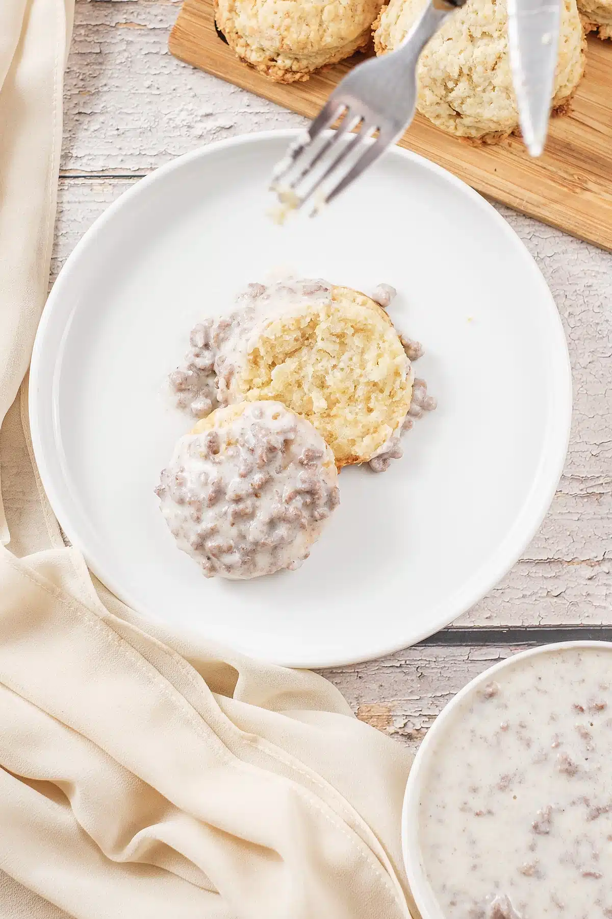 Sausage gravy spooned over two split biscuit halves with a fork alongside